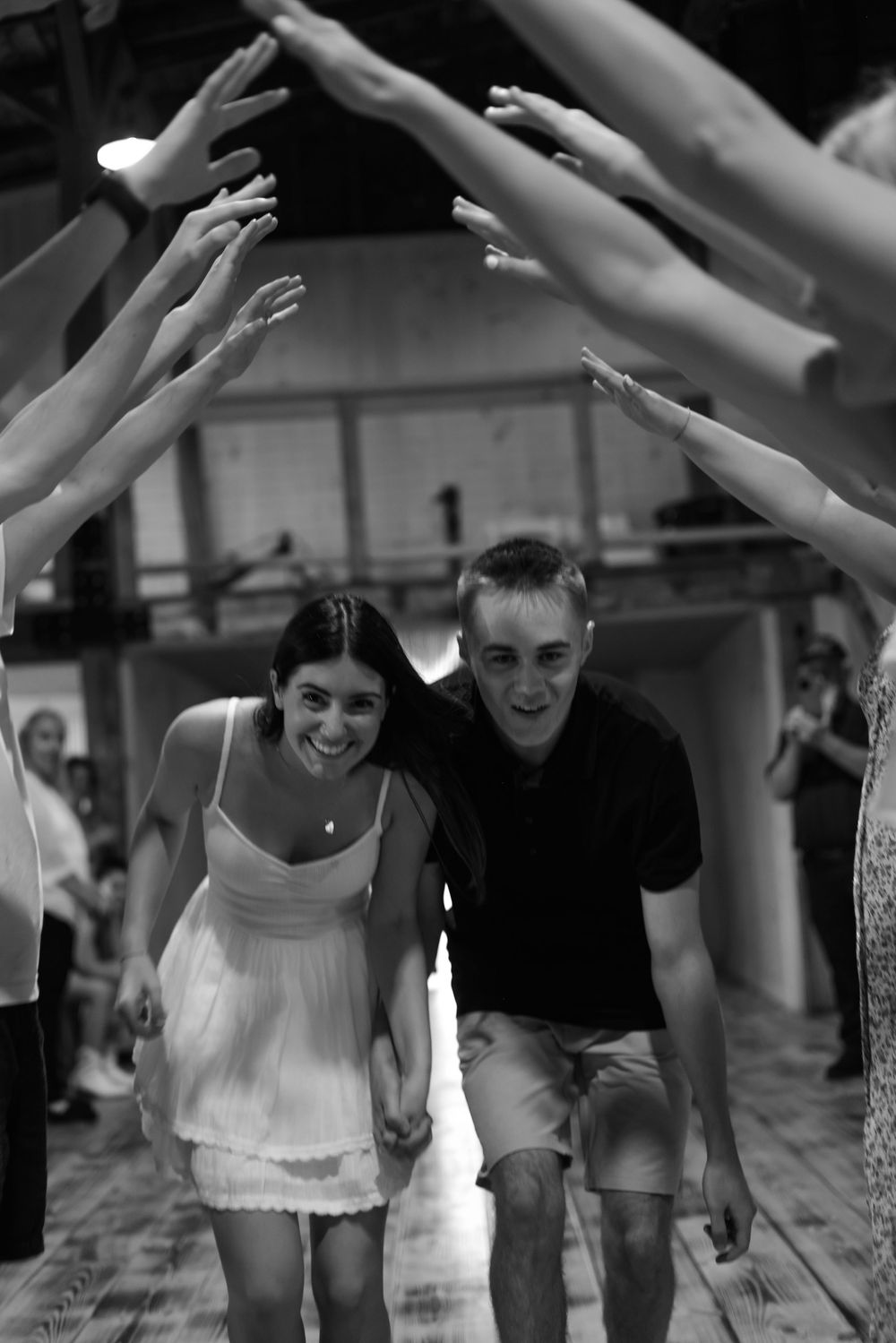 Black and white photo of newlyweds walking through raised hands tunnel at wedding reception.
