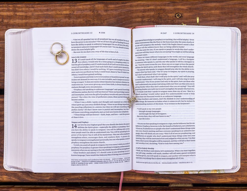 Gold wedding rings resting on open Bible showing 1 Corinthians passage.