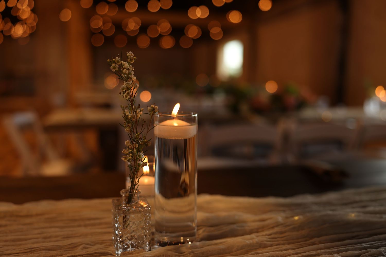 Elegant floating candle centerpiece in glass cylinder vase with bokeh lights at wedding reception.