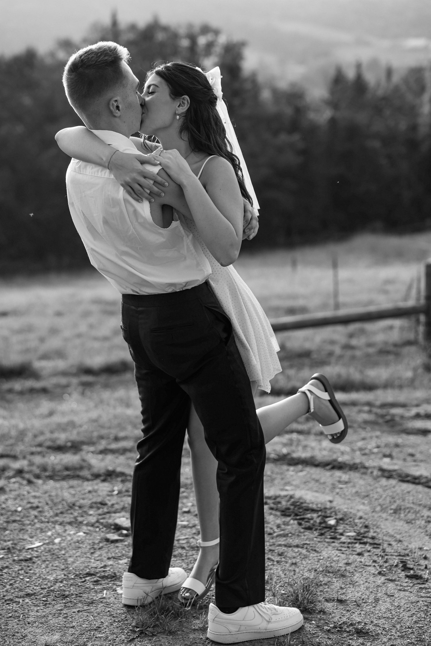 Black and white photo of groom lifting bride for a romantic kiss at outdoor wedding venue.