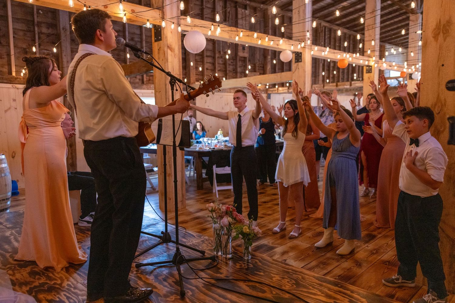 Wedding guests dancing and celebrating with live musician performing at rustic barn reception.