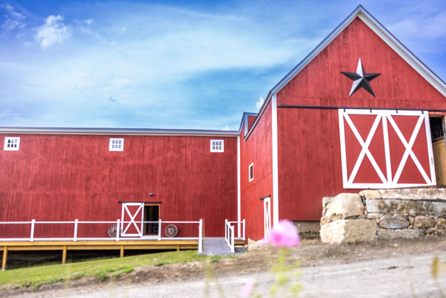 Red barn with white X doors and black star detail under a blue sky on a rustic farm.