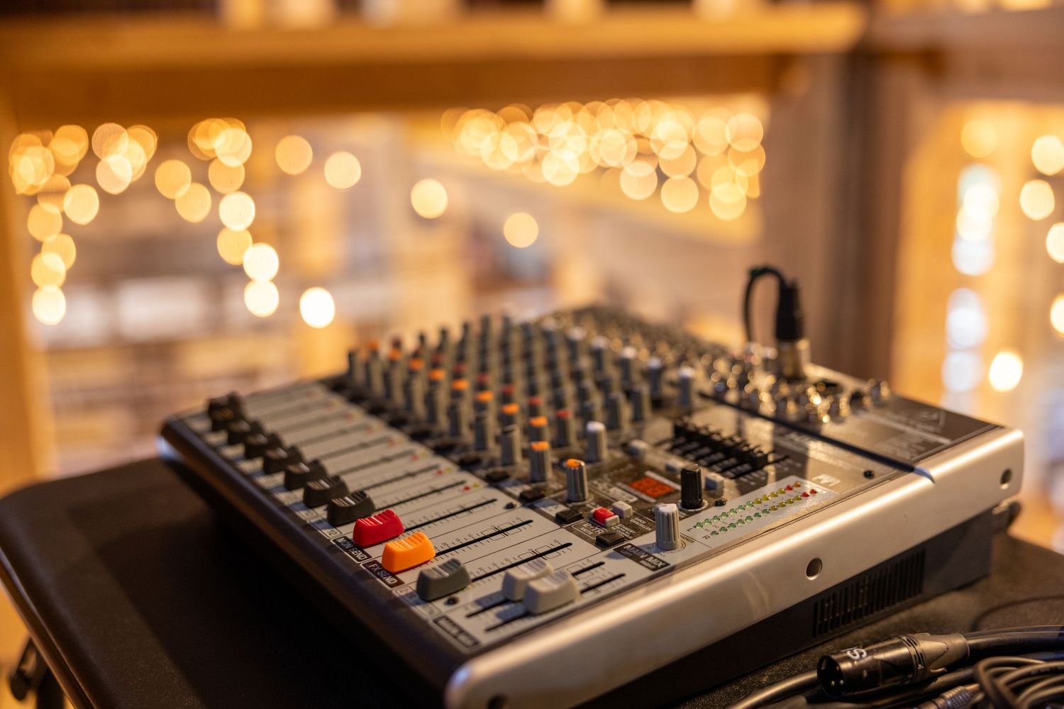 Professional audio mixing board with colorful knobs set up for wedding reception with bokeh lights behind.