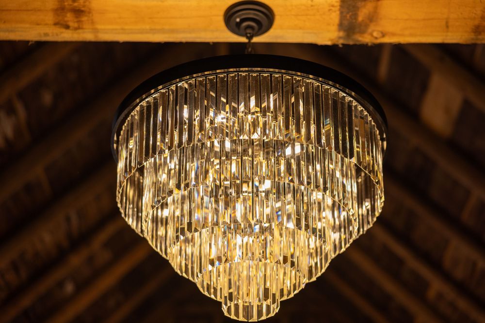 Elegant tiered crystal chandelier hanging from rustic wooden ceiling in a wedding venue barn.