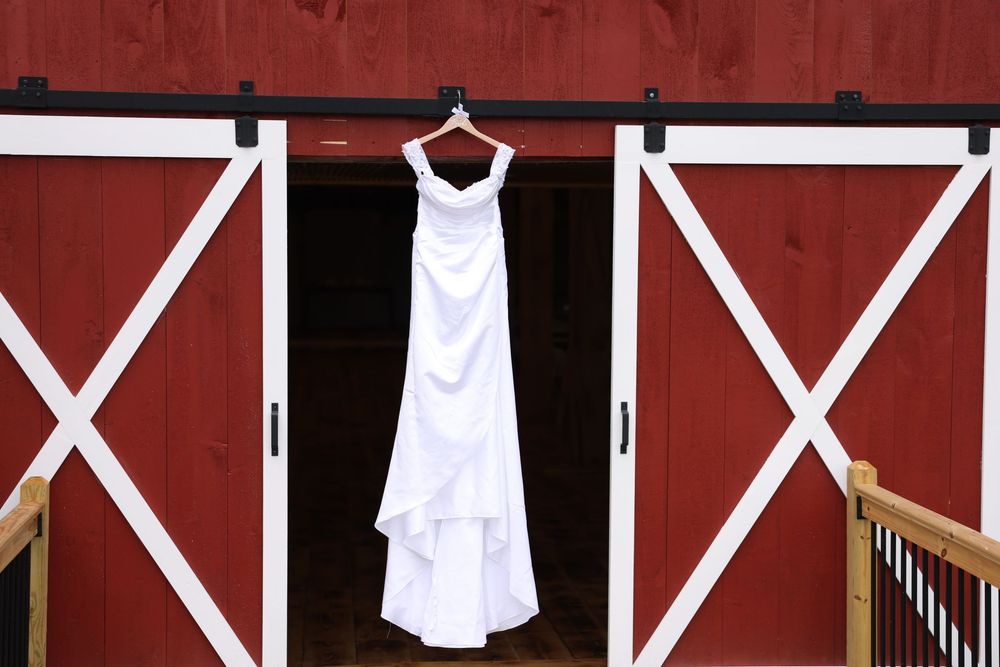 White wedding dress hanging on red barn sliding doors with white trim.