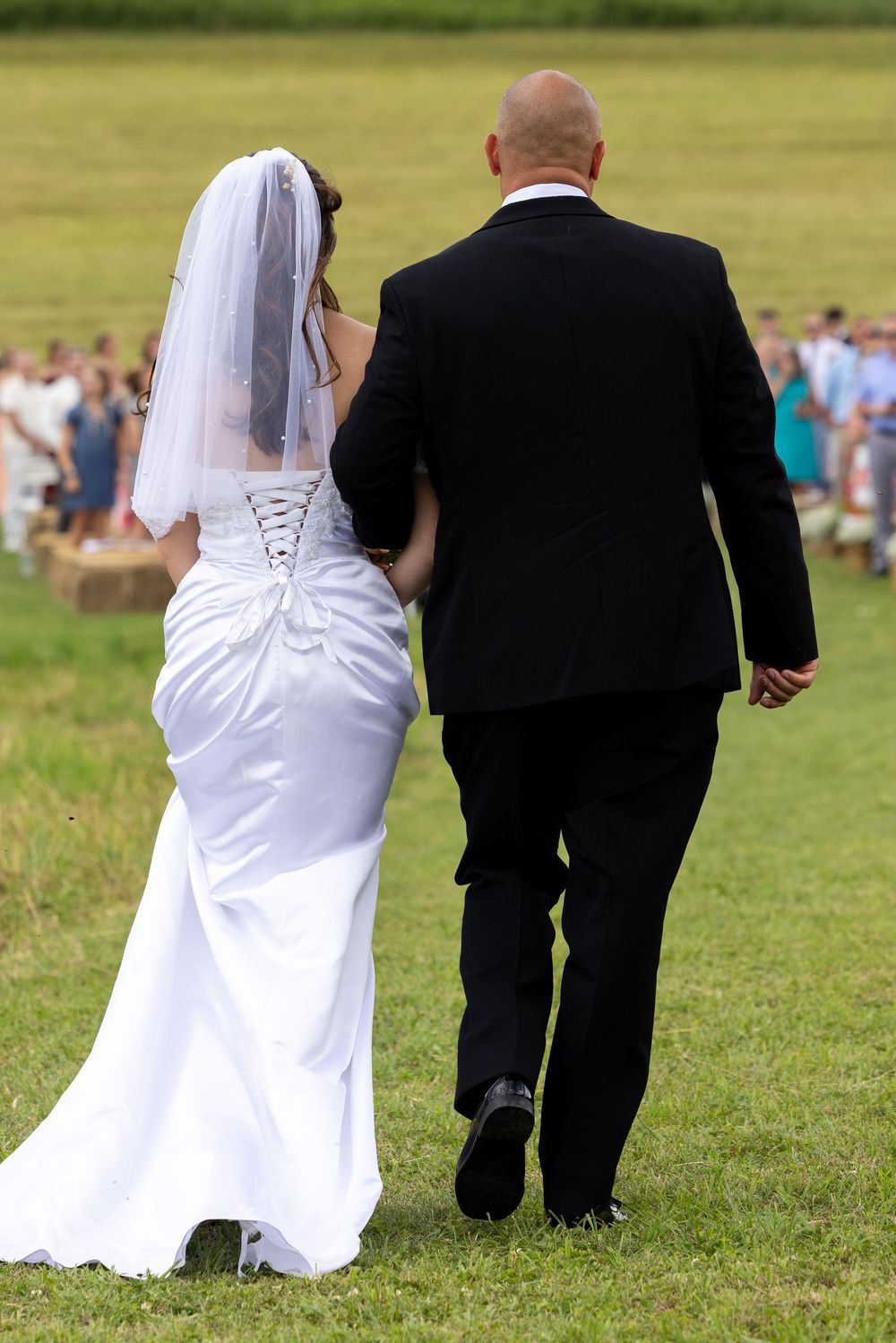 Bride and groom walking hand in hand across green grass at outdoor wedding.