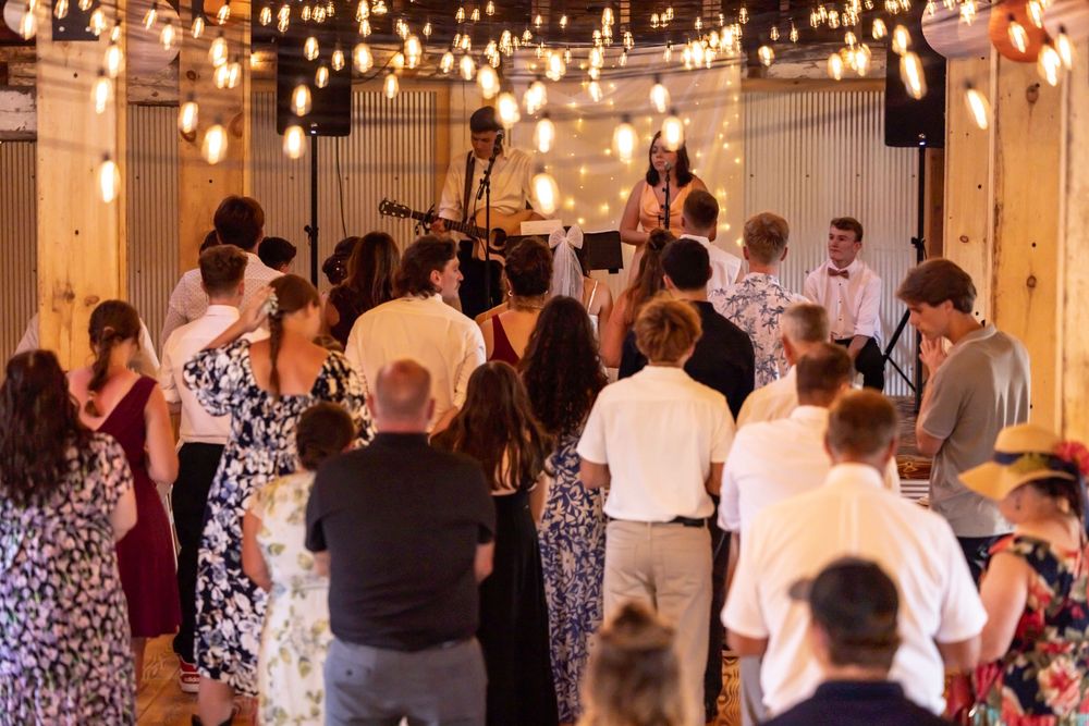 Wedding guests dancing under warm string lights inside a rustic barn venue.