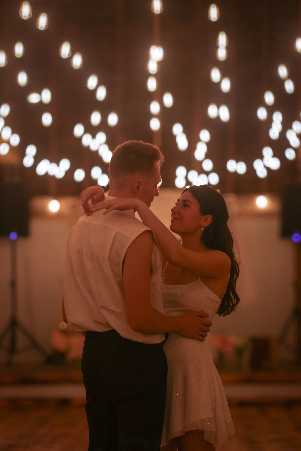 Couple sharing an intimate slow dance under warm bokeh string lights at a romantic wedding reception.