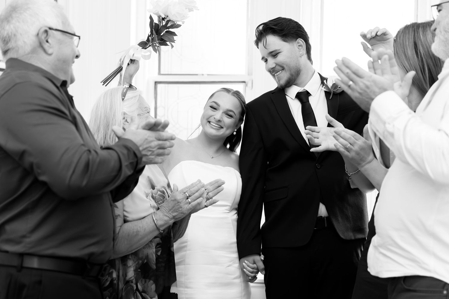 Bride and groom walking through applauding guests in black and white wedding ceremony photo.
