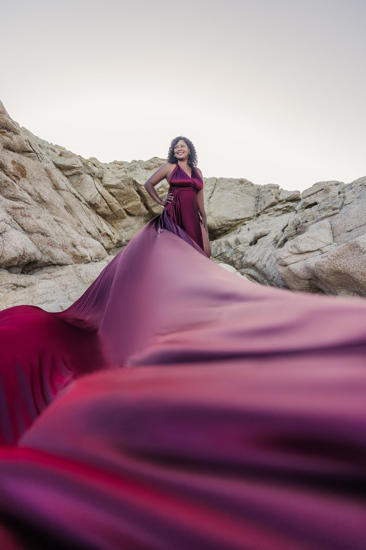 Woman in burgundy flowing dress posing among desert rock formations.
