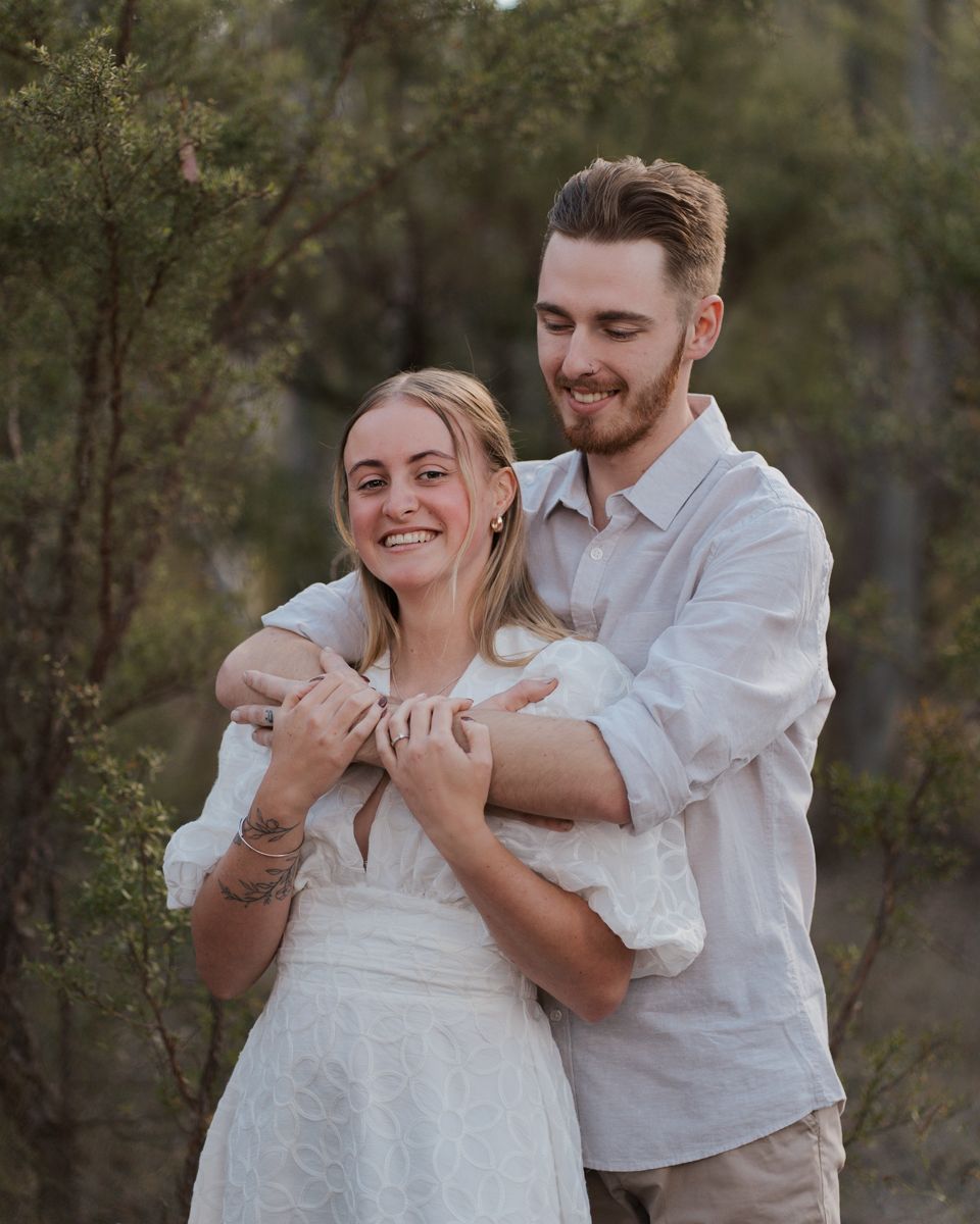 Happy couple outdoors in white outfits, smiling in a natural bush setting during golden hour engagement photoshoot in rouse hill