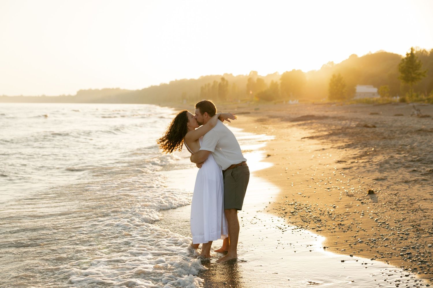 Couple embracing on beach at sunset with golden light and water in background.