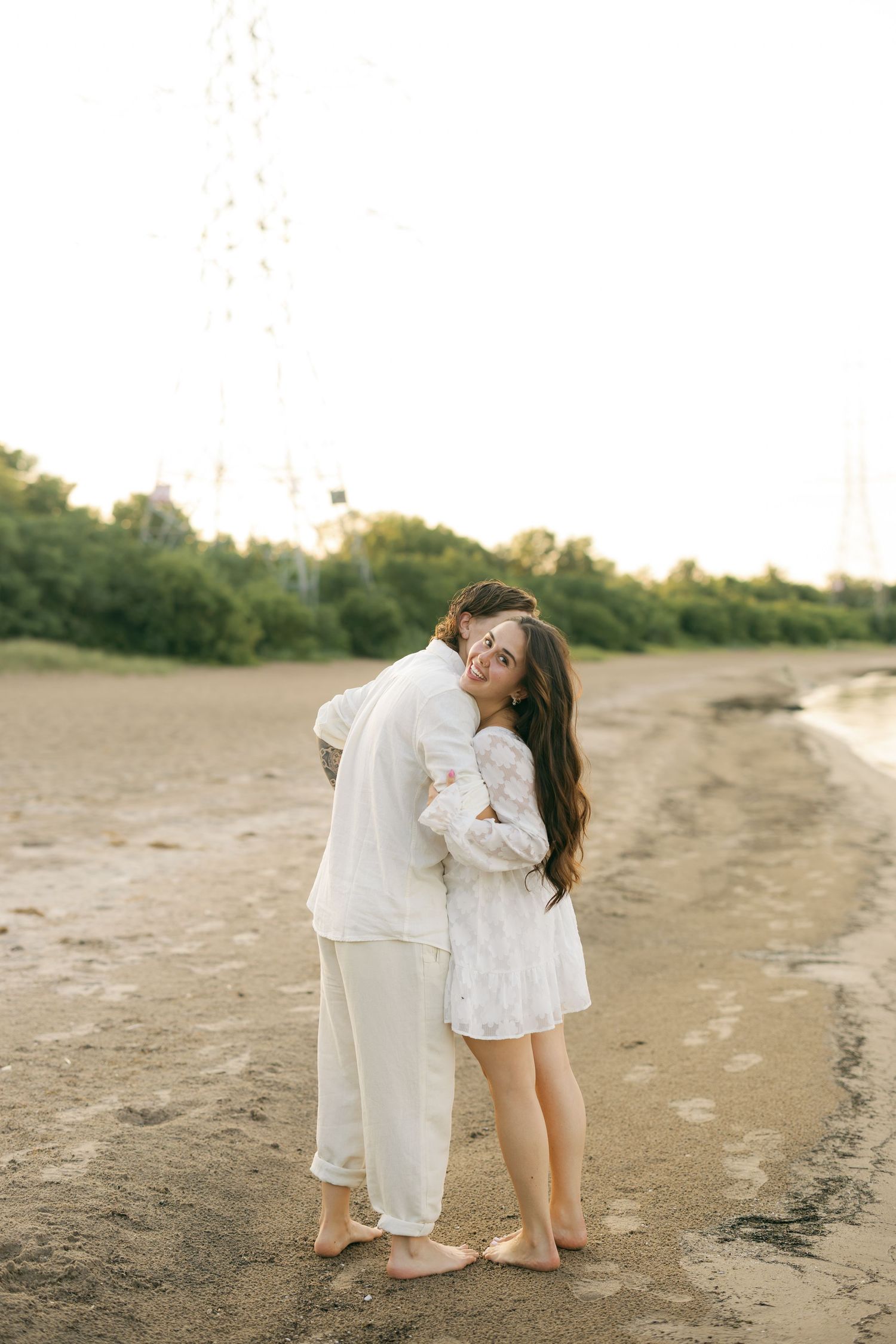 Couple sitting together on sandy beach dunes surrounded by autumn foliage on a cloudy day.