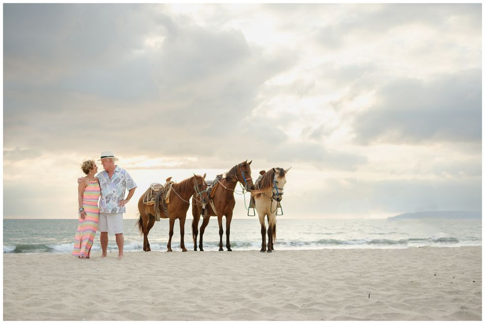 Beach couples photography at Villa del Palmar Flamingos with a couple and horses on the beach at sunset.