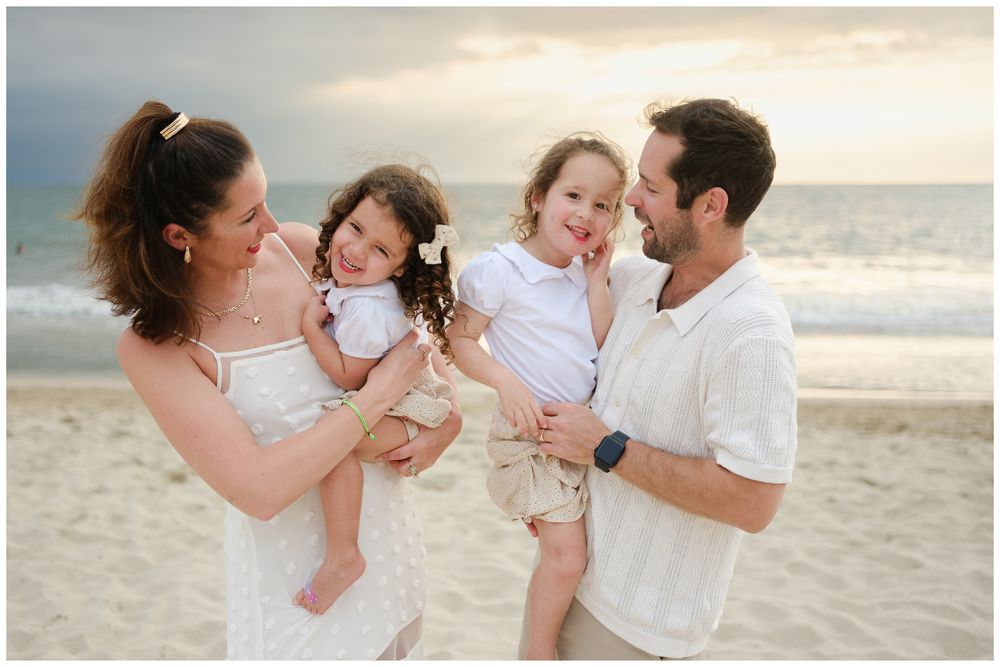 Beach family photos at Villa del Palmar Flamingos of a family of four holding their daughters at sunset.