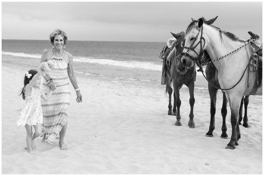 Beach family photos at Villa del Palmar Flamingos of a mother and child walking beside horses in black and white.