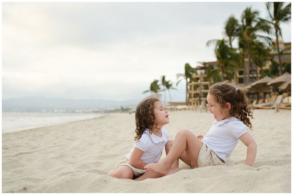 Beach family photos at Villa del Palmar Flamingos of two sisters sitting together on the sand near the resort.