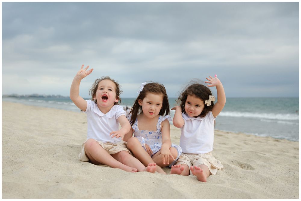 Beach family photos at Villa del Palmar Flamingos of three sisters sitting on the sand waving at the camera.