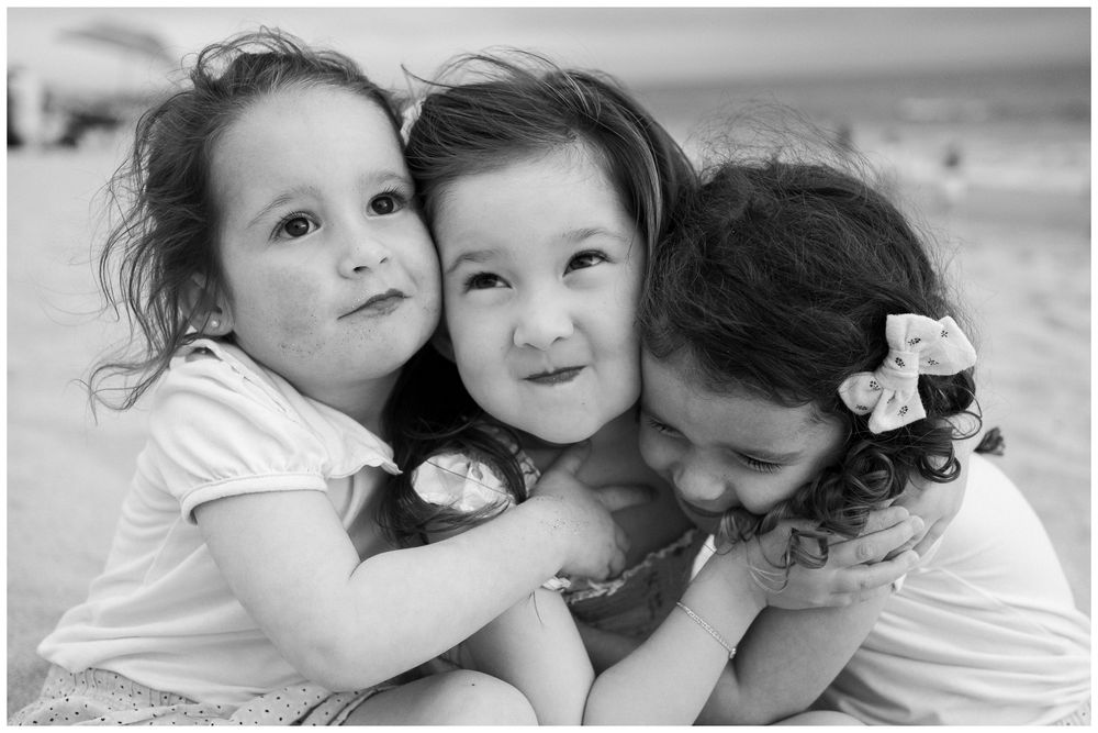 Beach family photos at Villa del Palmar Flamingos of three sisters hugging together in a black and white portrait.