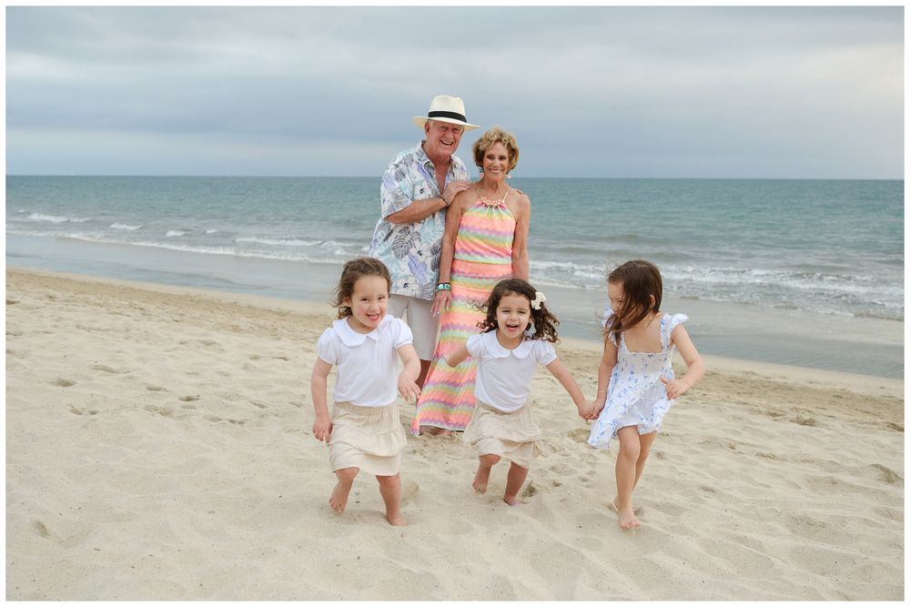 Beach family photos at Villa del Palmar Flamingos of grandparents with three granddaughters holding hands by the ocean.