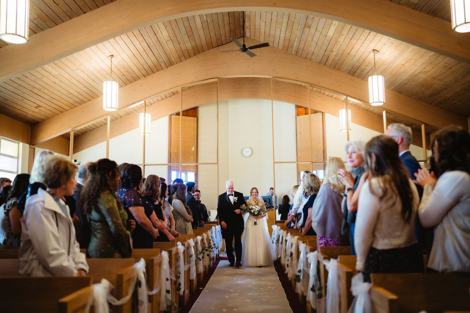 Bride walking down the aisle with escort in a wooden chapel church during a wedding ceremony.