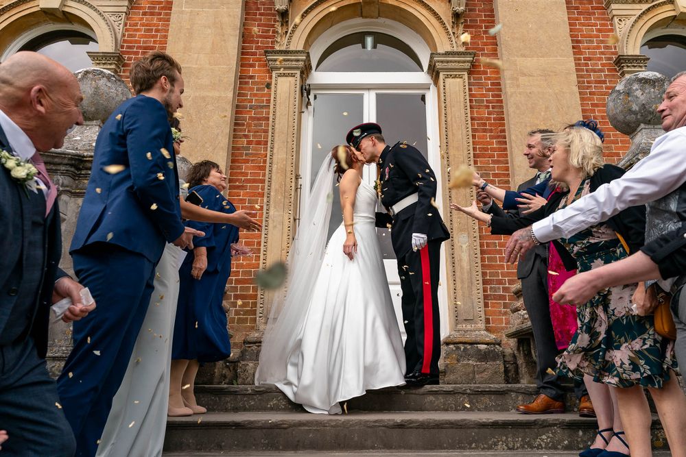 Bride and Groom kiss whilst guests throw confetti at Crowcombe Court