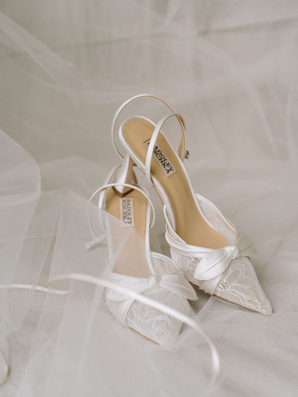 White lace Badgley Mischka bridal heels with bow detail and slingback strap on soft tulle fabric.