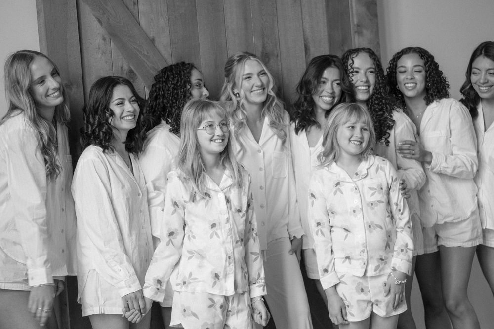 Black and white photo of a group of women in matching pajamas smiling and laughing together indoors.