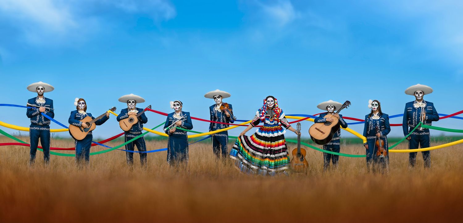 Mariachi band in traditional charro suits and sombreros with a dancer in colorful dress in a golden field.