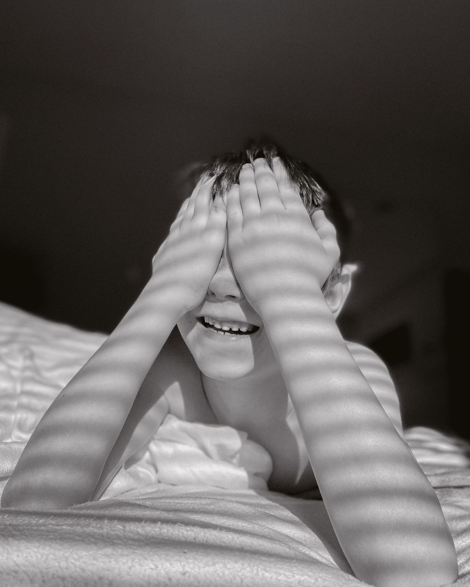 Black and white photo of a young boy holding hands over his eyes and smiling