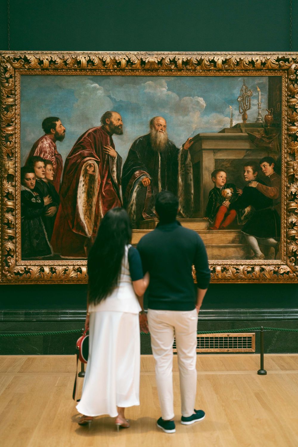 Couple viewing a large Renaissance painting in a museum gallery with green walls.