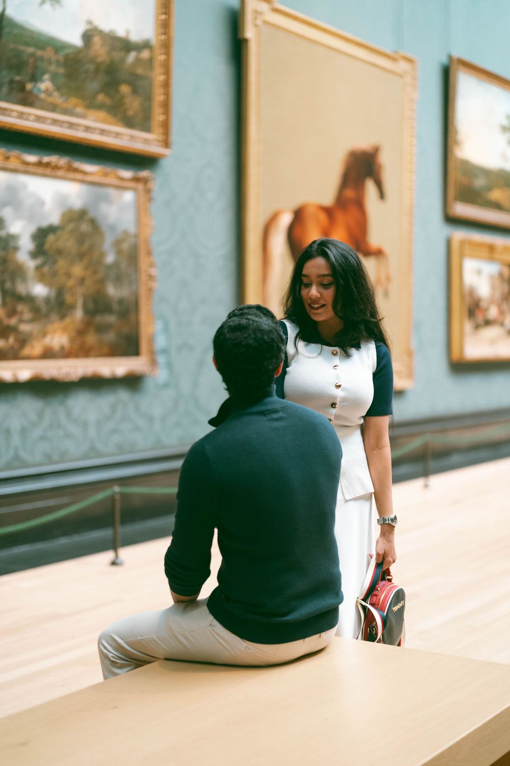 Couple sharing a romantic moment in an art museum gallery with classic paintings on blue walls.