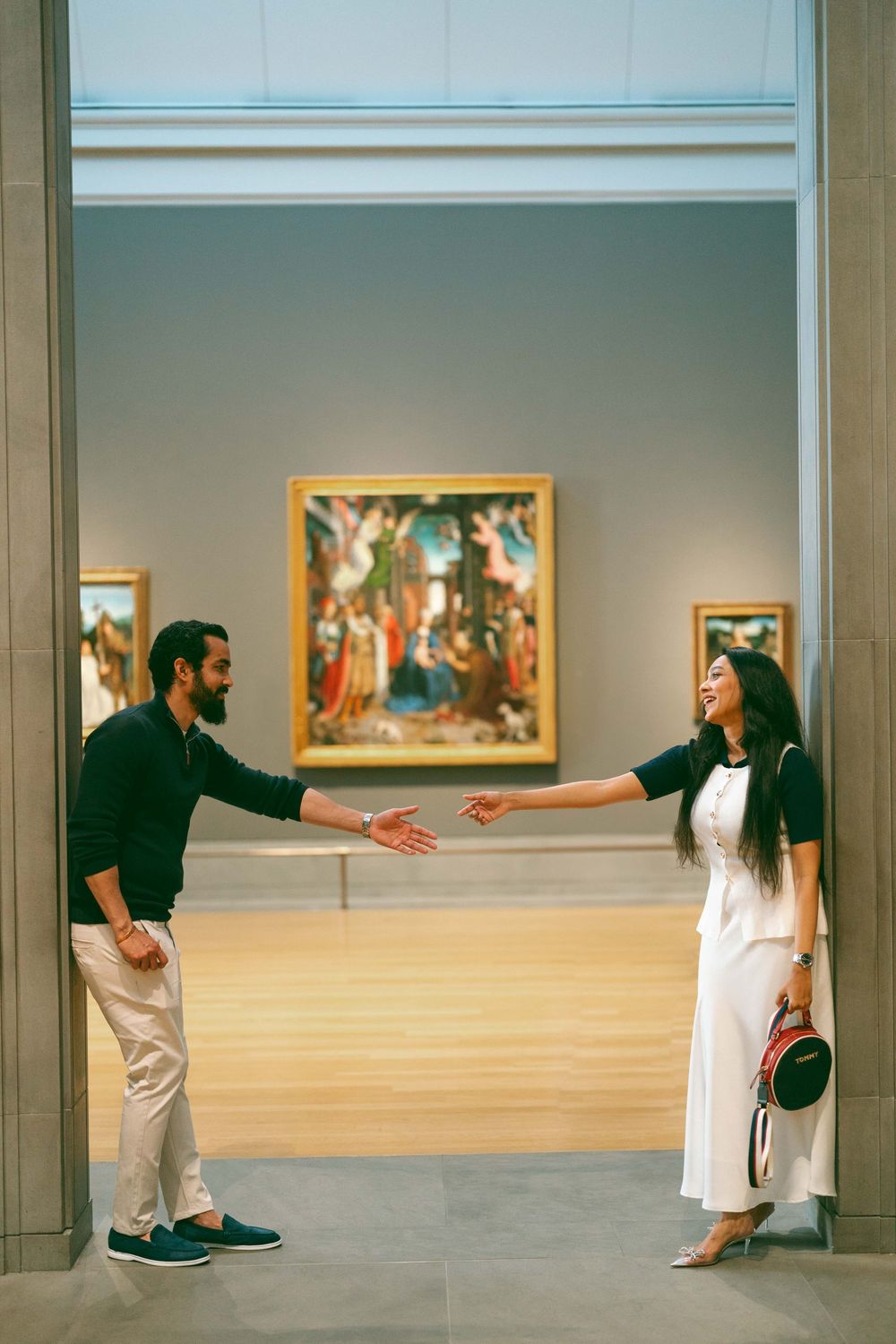 Couple reaching toward each other in an art museum gallery with colorful Renaissance paintings on display.