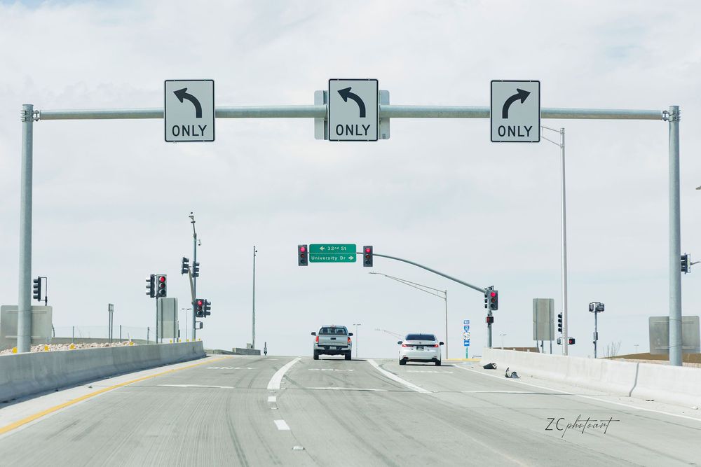 A multi-lane highway intersection with three overhead turn-only signs directing left and right traffic under a cloudy sky.