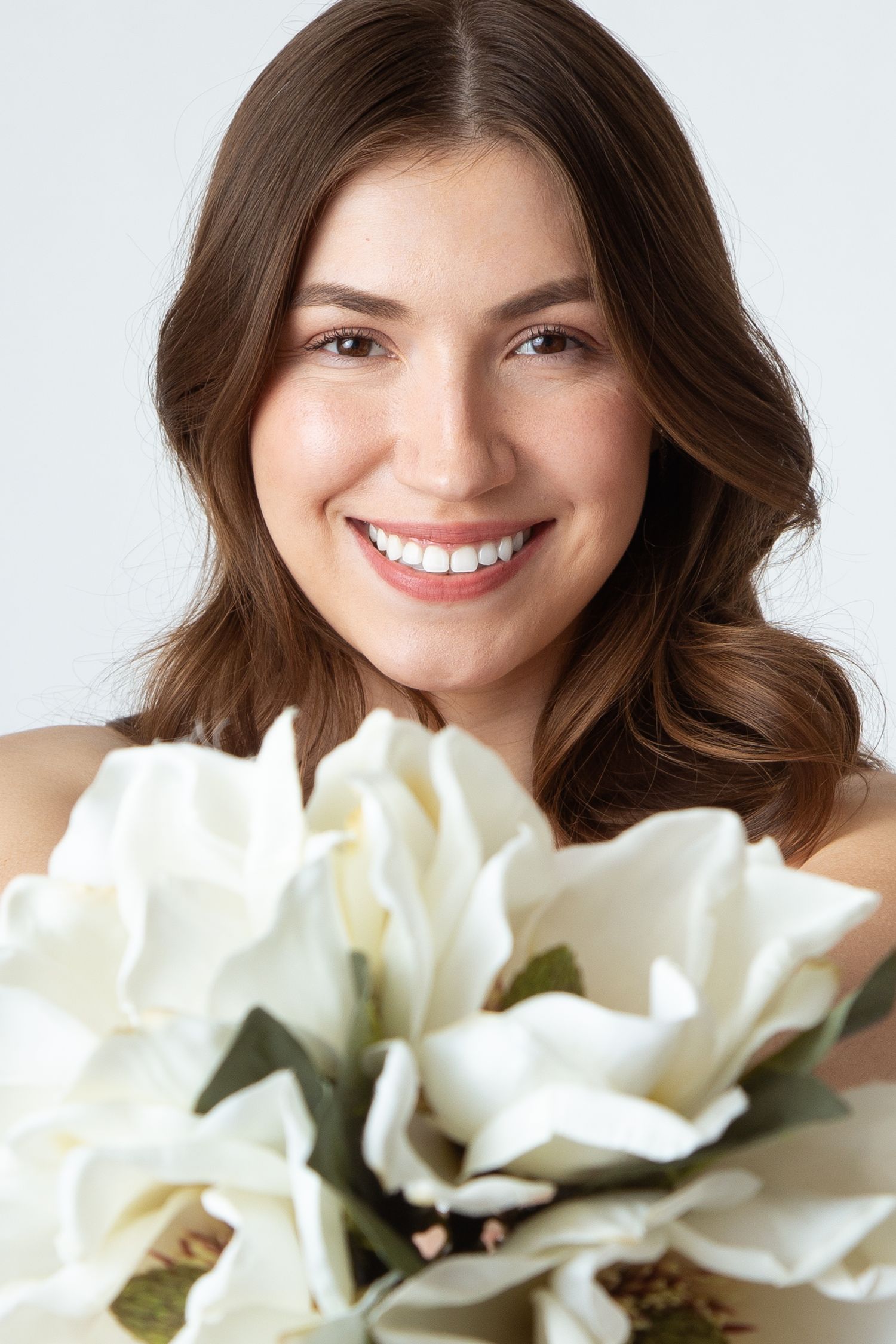 Close up photo of a brunette bride smiling with a bouquet of white magnolia flowers at Celebrations Bridal and Prom in New Braunfels Texas.