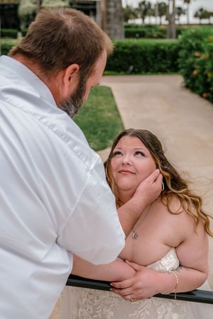 Groom tenderly holds bride's face as she gazes up at him adoringly on an outdoor walkway.