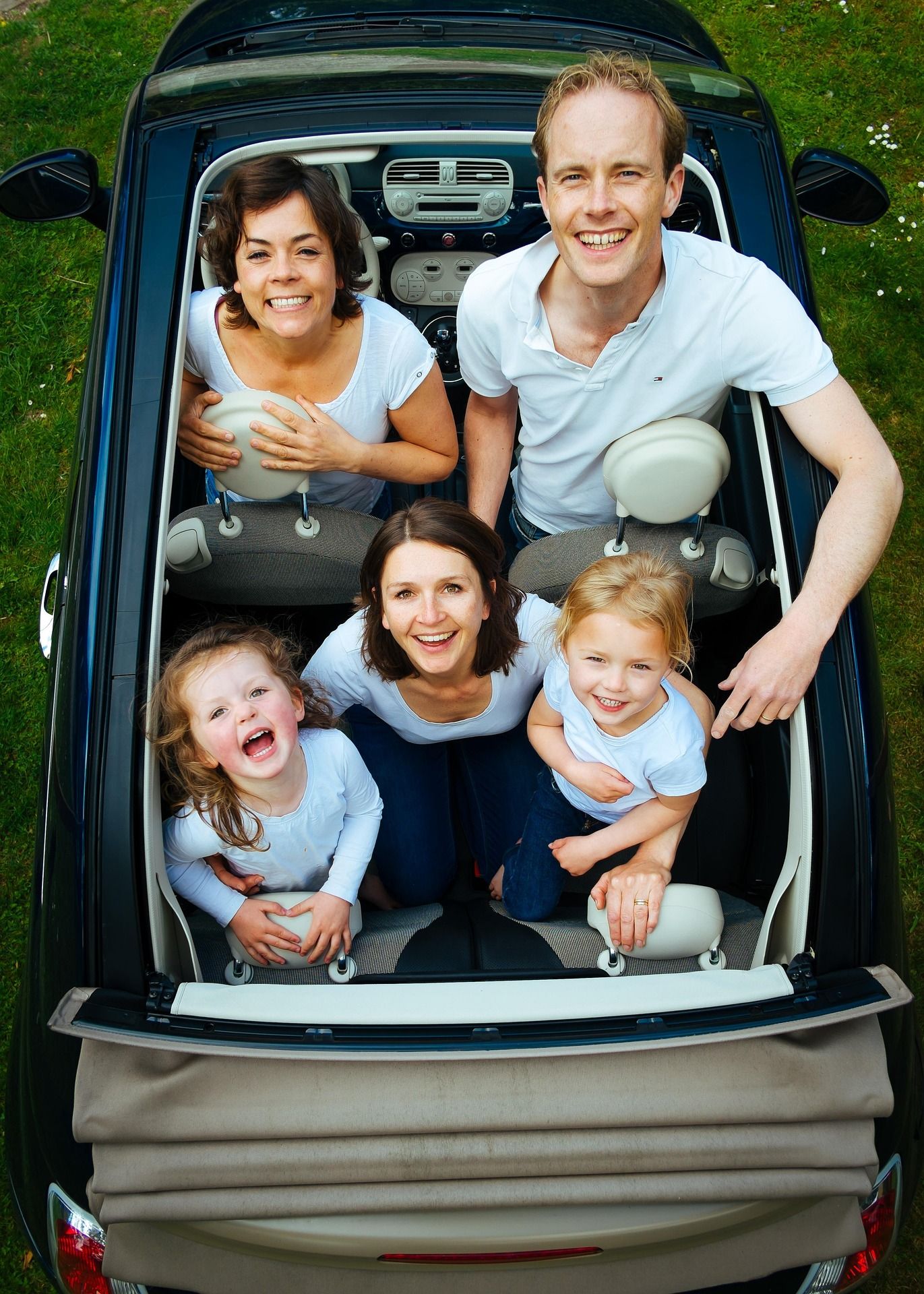 Vue aérienne d'une famille heureuse de cinq personnes souriant à l'intérieur d'une voiture décapotable garée sur de l'herbe verte