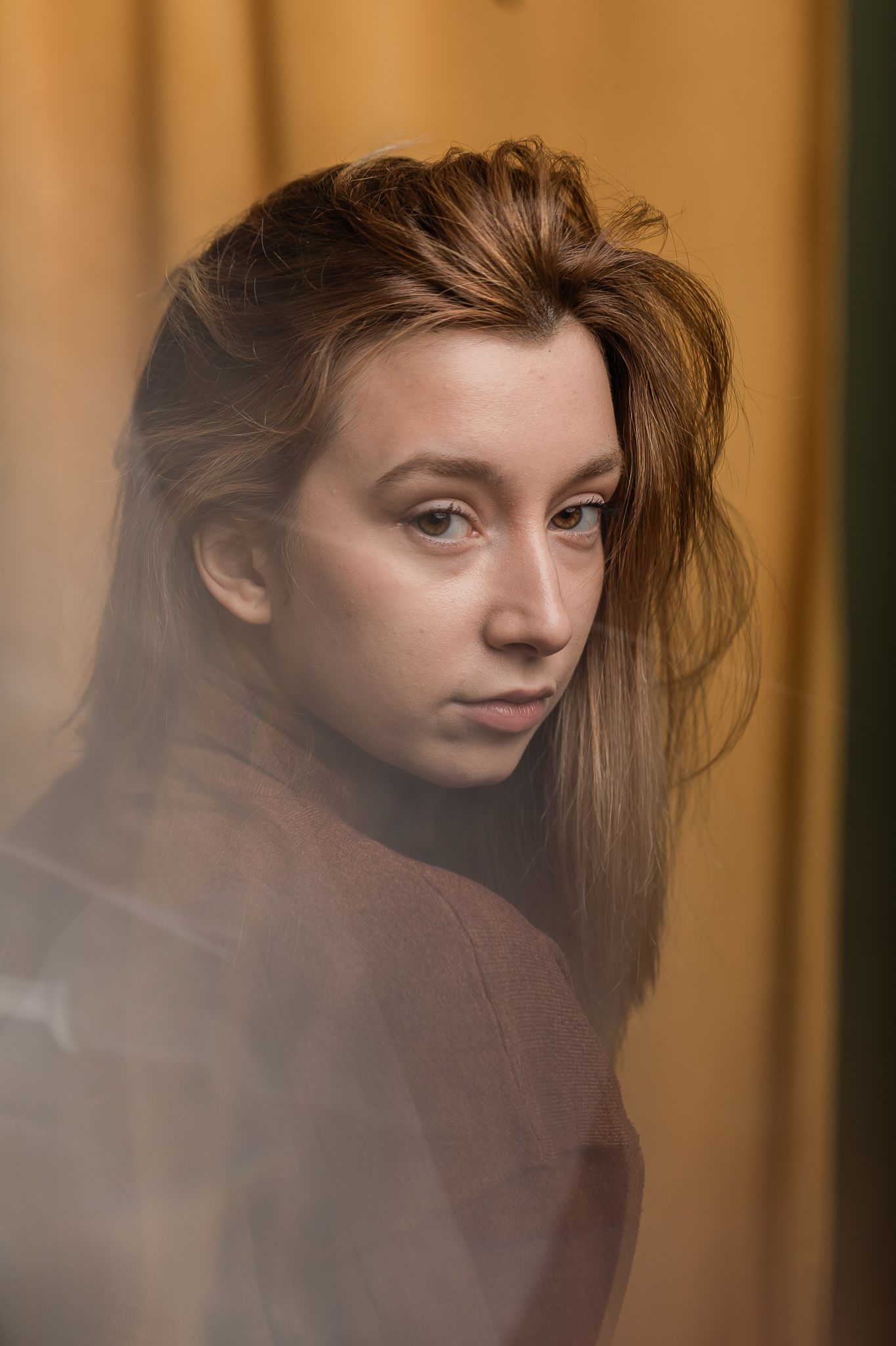 Artistic portrait with soft lighting shows a dramatic over-the-shoulder pose against a warm brown background.