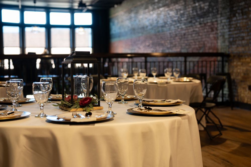 An elegant restaurant table with white tablecloth and place settings against exposed brick walls in ambient lighting.