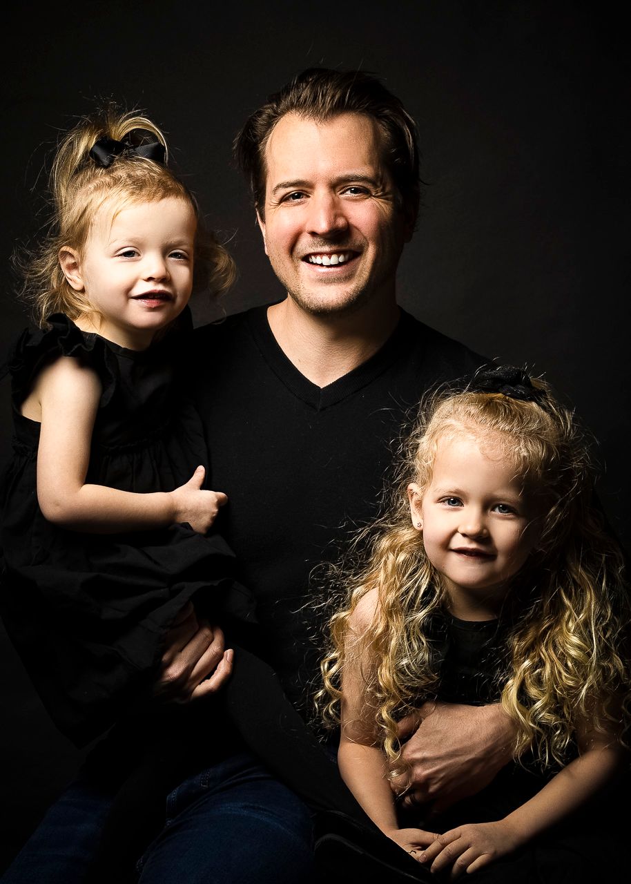 Heartwarming family studio portrait against dark background showing joyful expressions in matching black attire.