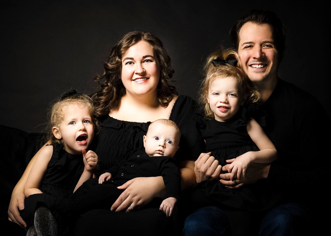 Studio family portrait with four children and parents wearing black clothes against dark background.