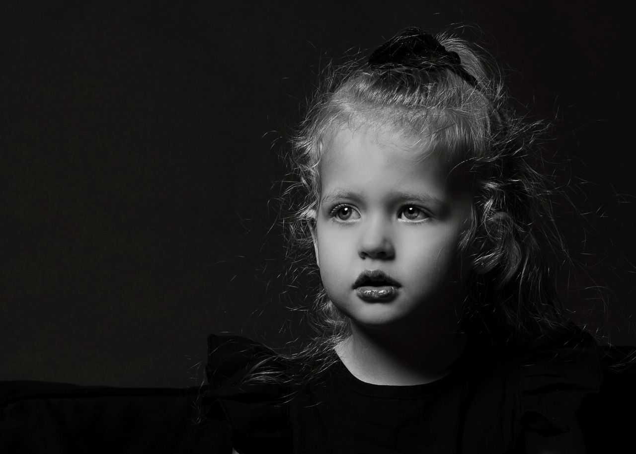 Dramatic black and white portrait of a child against dark background with ethereal lighting and wispy hair.