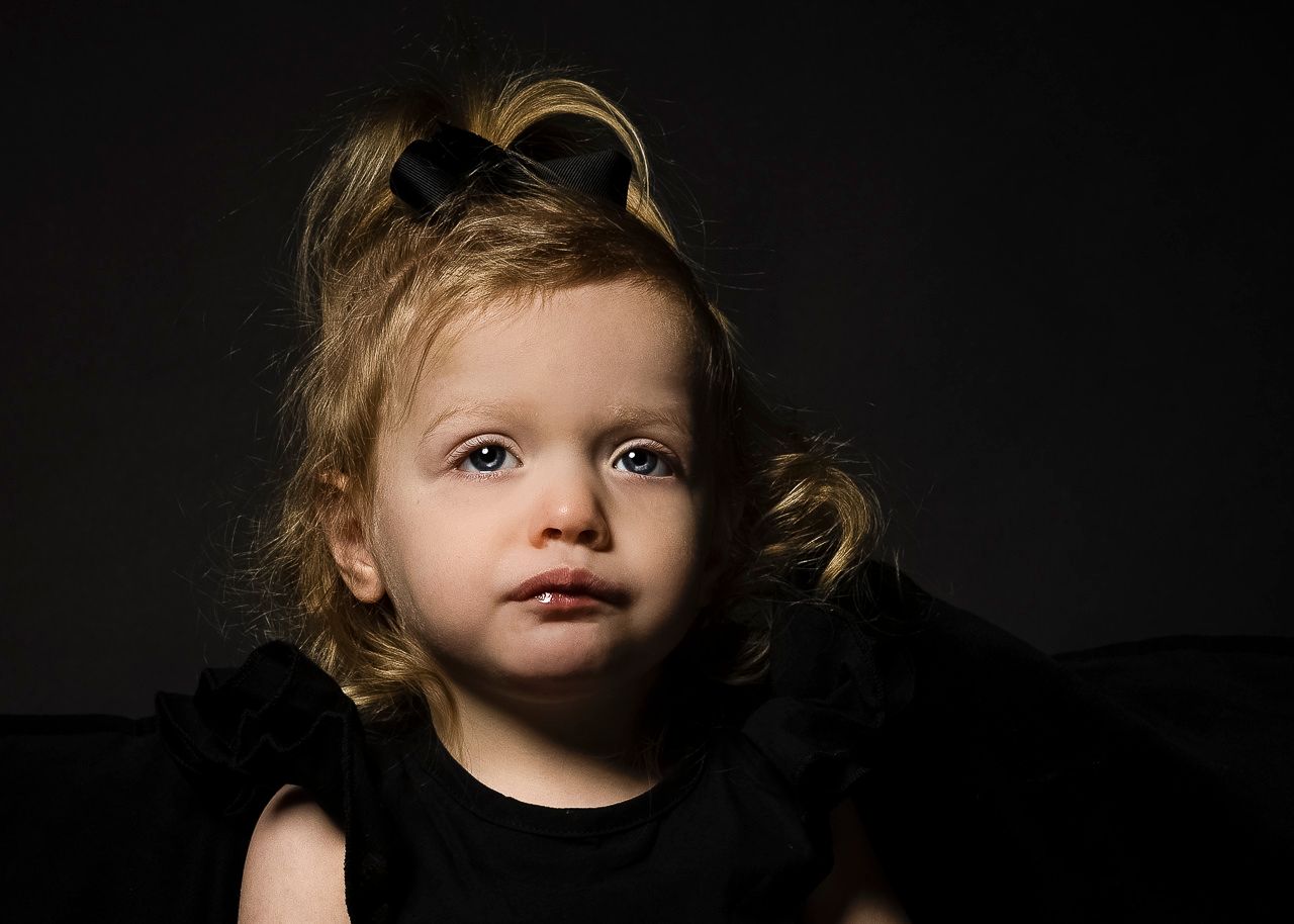 A young child wearing black against a dark background poses for a dramatic studio portrait.