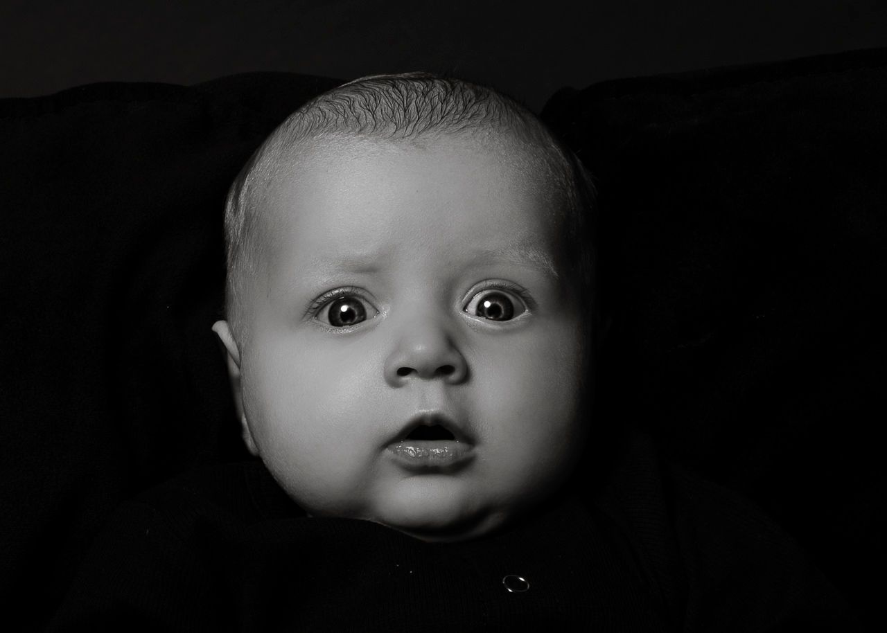 High contrast black and white close-up of an infant's face with bright eyes against a dark background.
