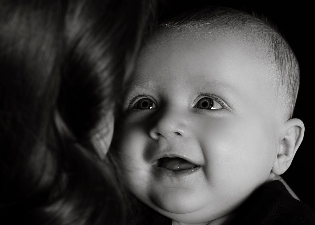 Black and white portrait of smiling baby with bright eyes looking up towards someone off camera.