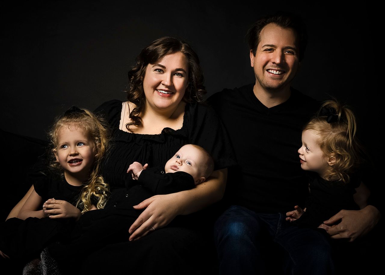 A family of five wearing black poses for a classic portrait against a dark background.