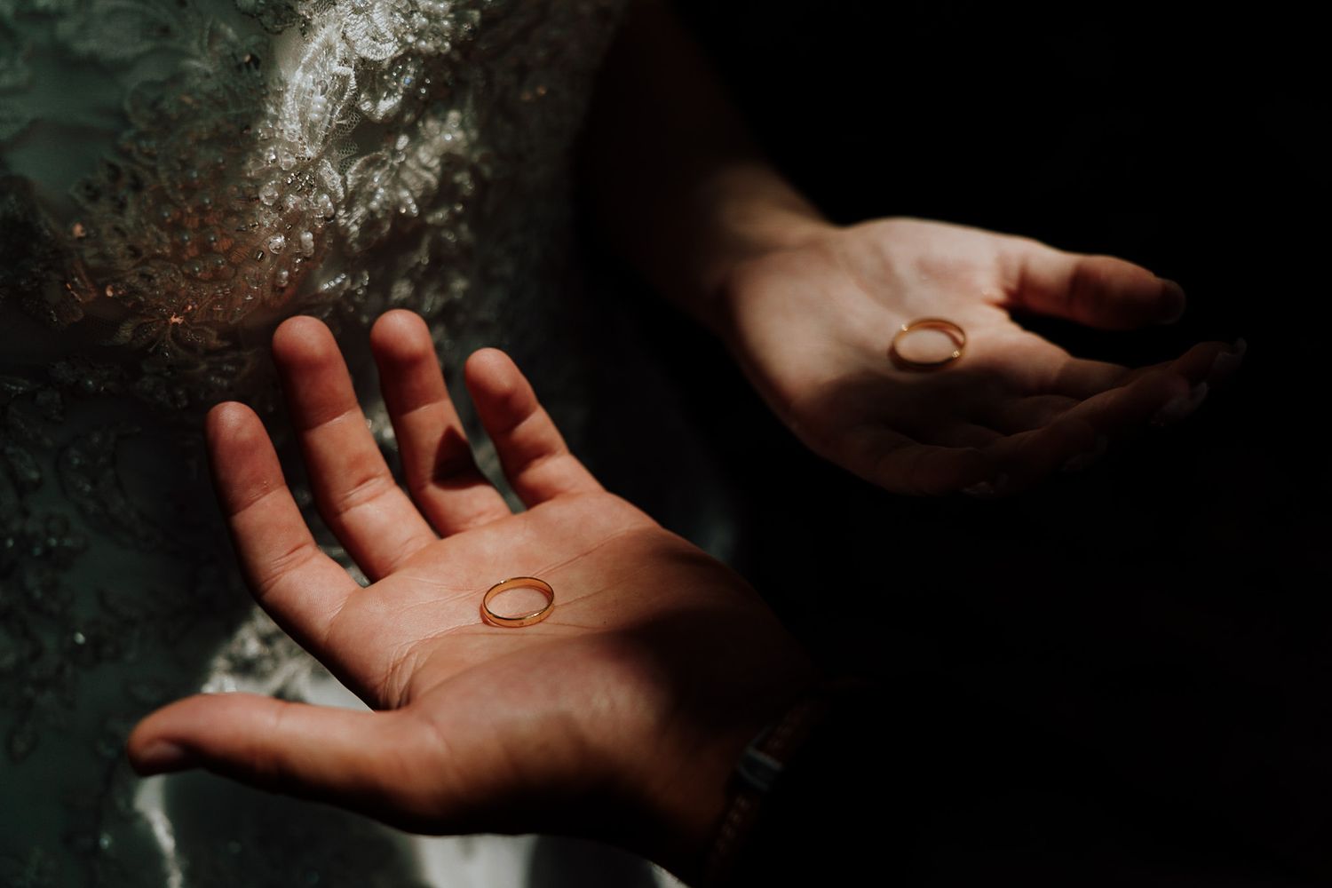 Wedding rings resting in open palms shot in dramatic lighting against a dark background.