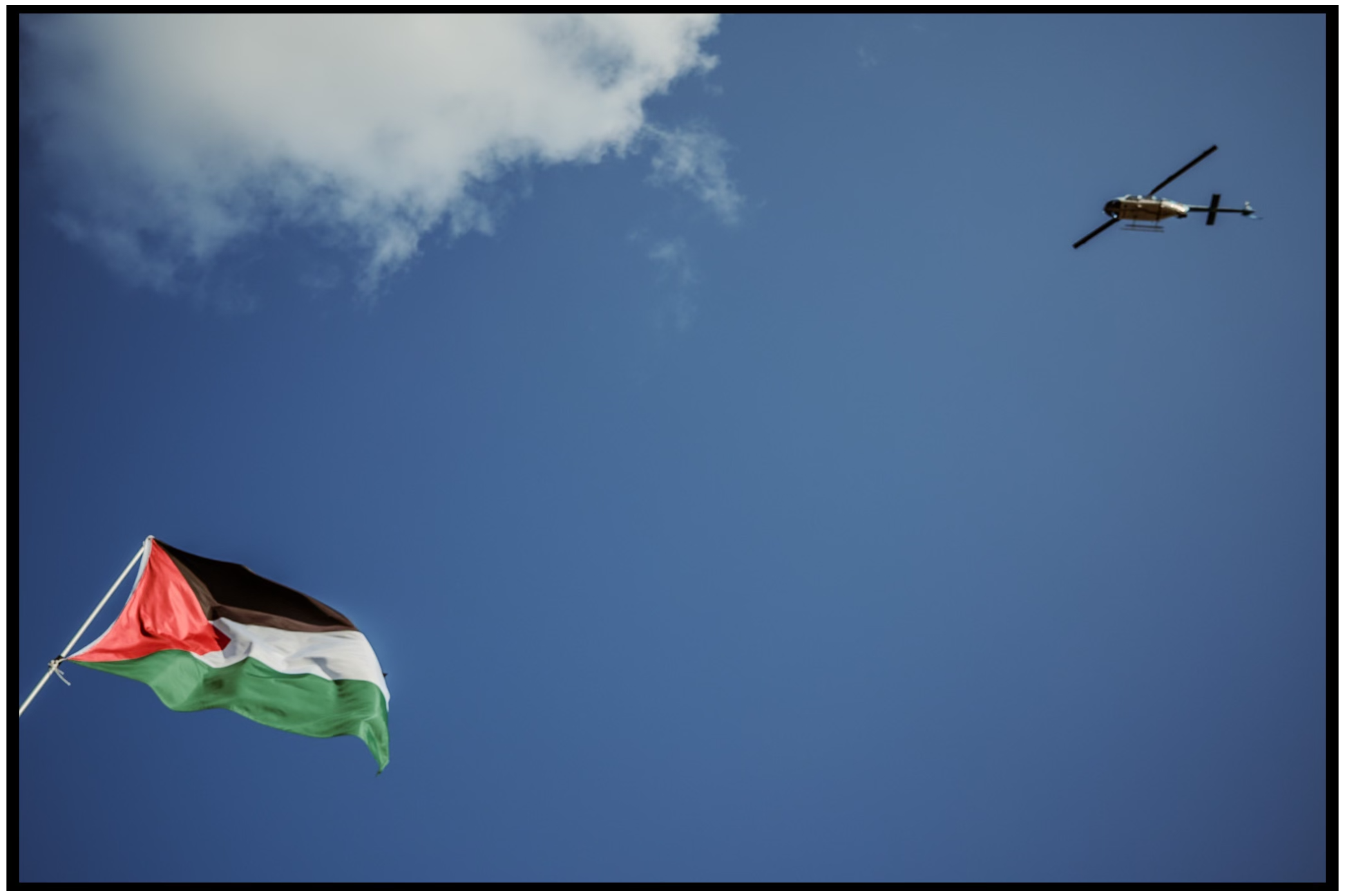 Palestinian flag waves against blue sky with helicopter flying overhead. Chicago. March on DNC