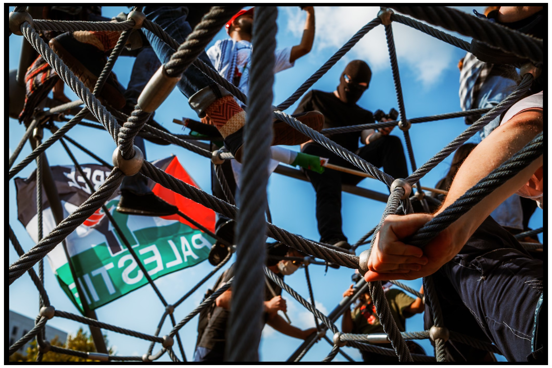 Low angle view of protesters climbing on metal framework with flags. Chicago. March on DNC