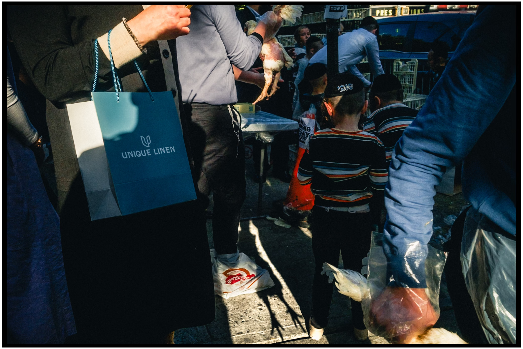 Street scene with shopping bags and people's legs visible in natural lighting. Kapparot, Brooklyn NYC